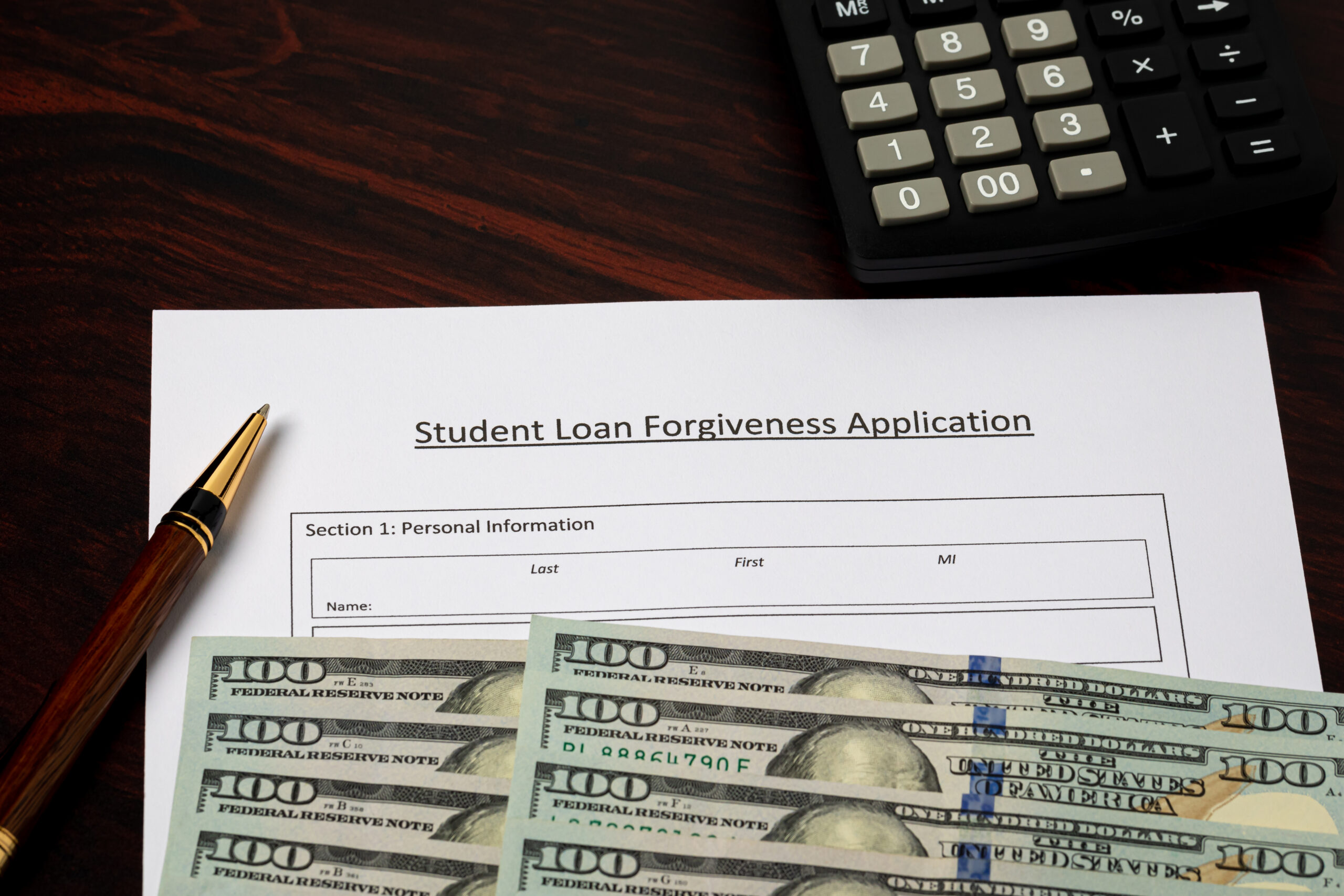 one hundred dollar bills on top of student loan forgiveness application paper