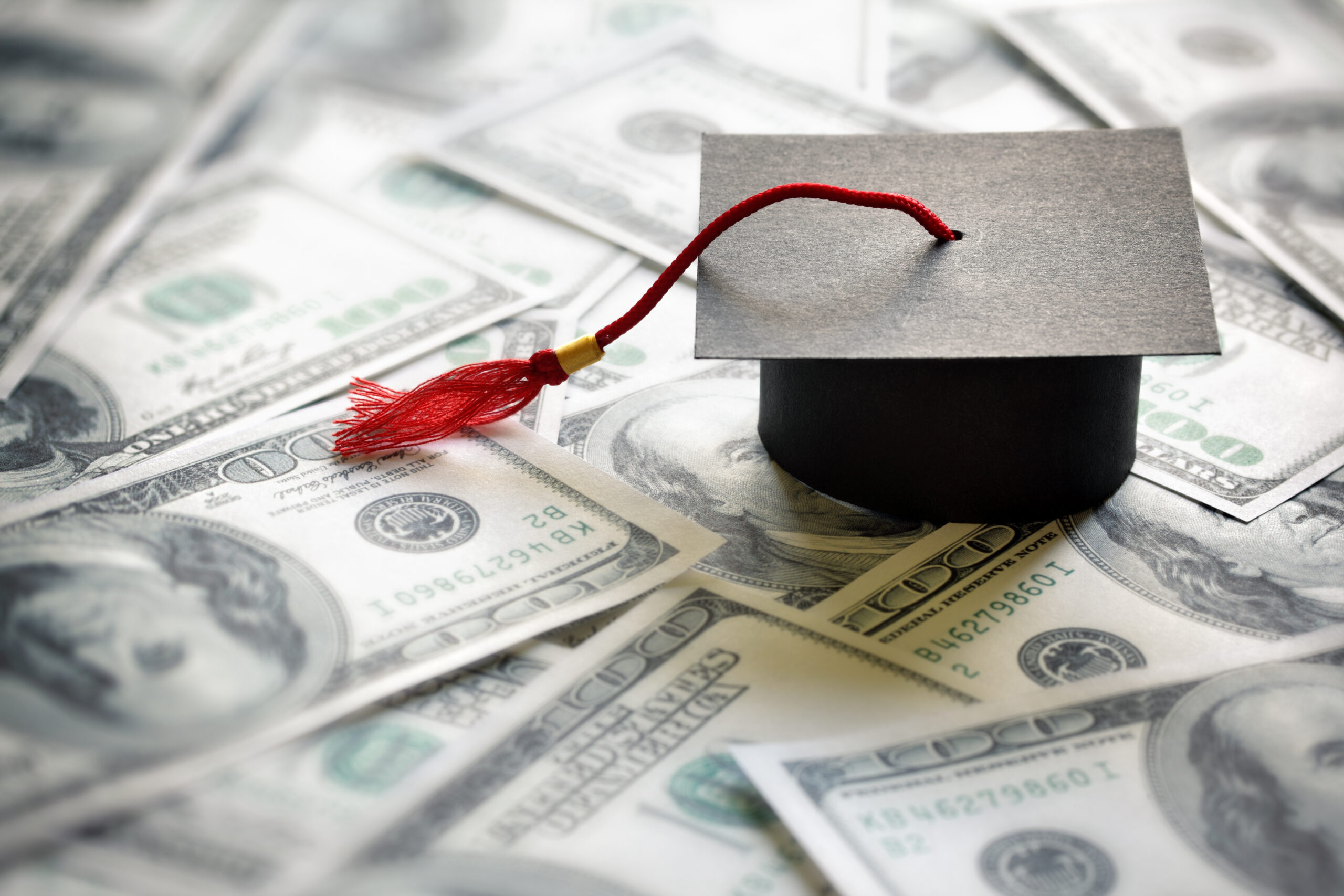 graduation cap on top of hundred dollar bills