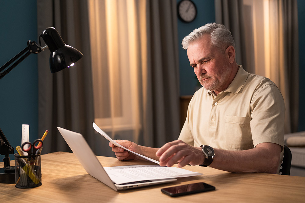 man looking at paperwork while at laptop